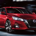 A red 2021 Nissan Altima is driving through a city at night after leaving a Nissan Altima Dealer.