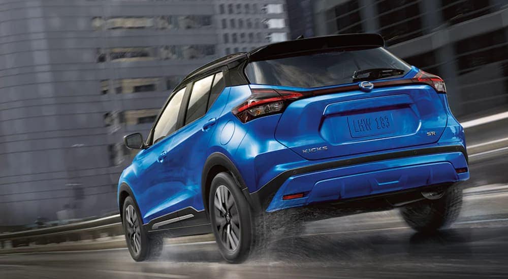 A blue 2021 Nissan Kicks is driving through a city in the rain.