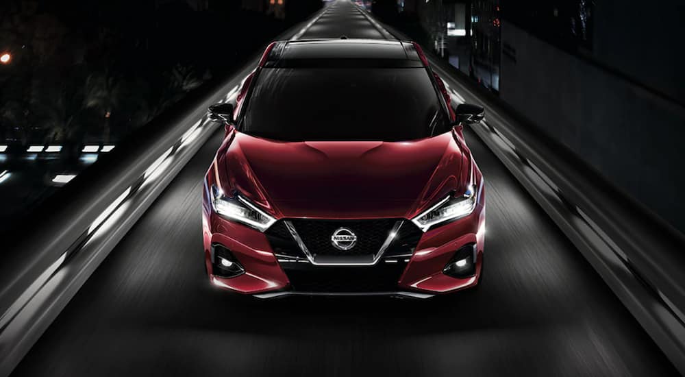 A red 2021 Nissan Maxima is shown driving from the front after leaving a Nissan dealership.
