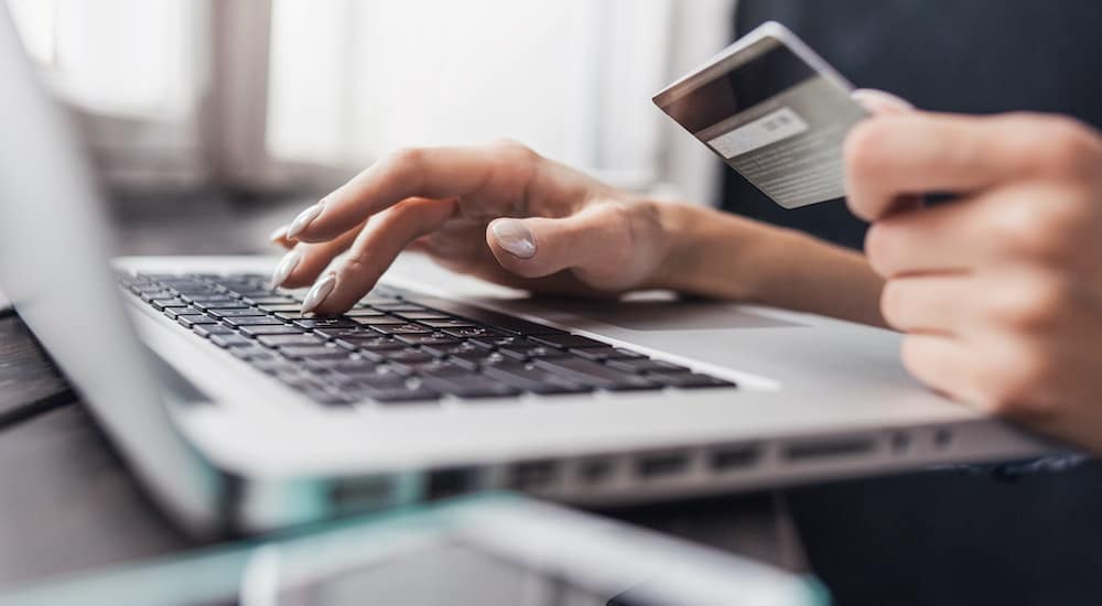 A woman is typing her credit card information into a computer after searching for online car dealers.