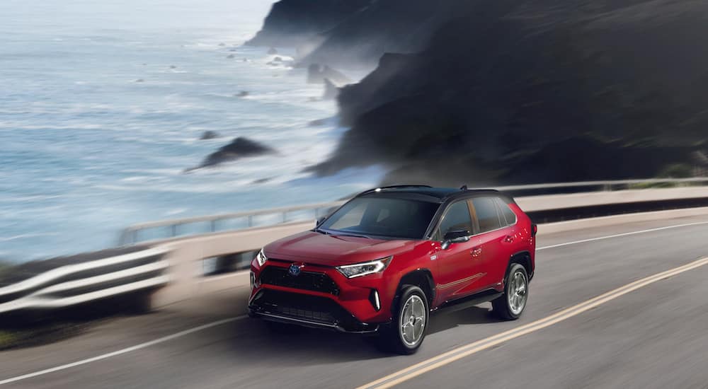 A red 2021 Toyota RAV4 Prime is driving past a lake after leaving a Toyota RAV4 dealership.