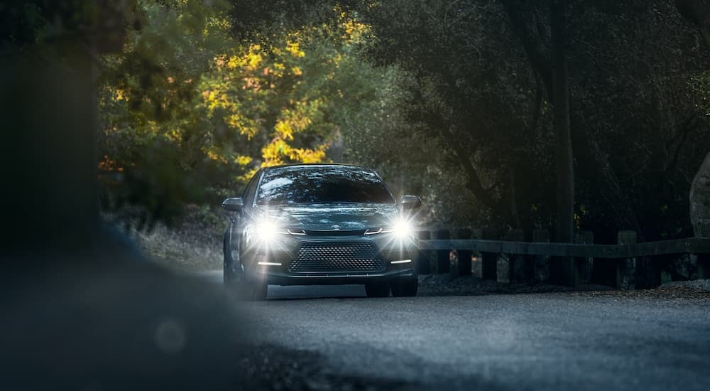 A blue 2021 Toyota Corolla XSE is shown driving past a guard rail with its headlights on.