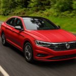 A red 2021 Volkswagen Jetta R-Line is shown driving down a wooded road after leaving a VW Jetta dealer.