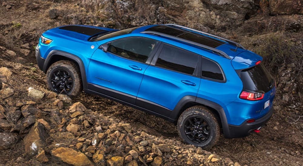 A blue 2020 Jeep Cherokee Trailhawk is off-roading on a rocky dirt hill.