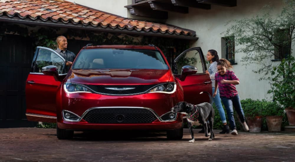 A red 2018 used Chrysler Pacifica is parked in a driveway as a family fills into the car.