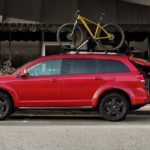 A used red 2020 Dodge Journey is parked in front of a hotel with a bike on the roof.