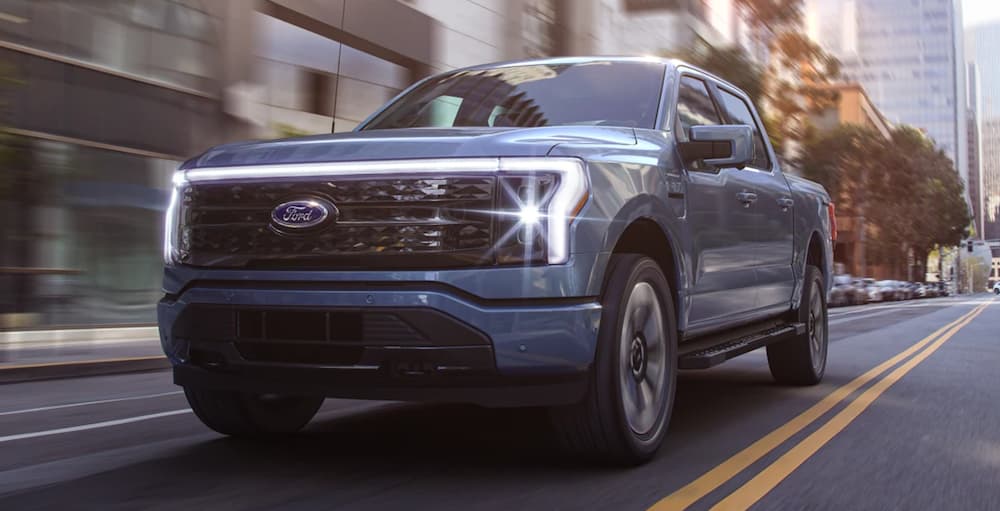 A blue 2022 Ford F-150 Lightning is shown driving through a city after leaving a used truck dealership.