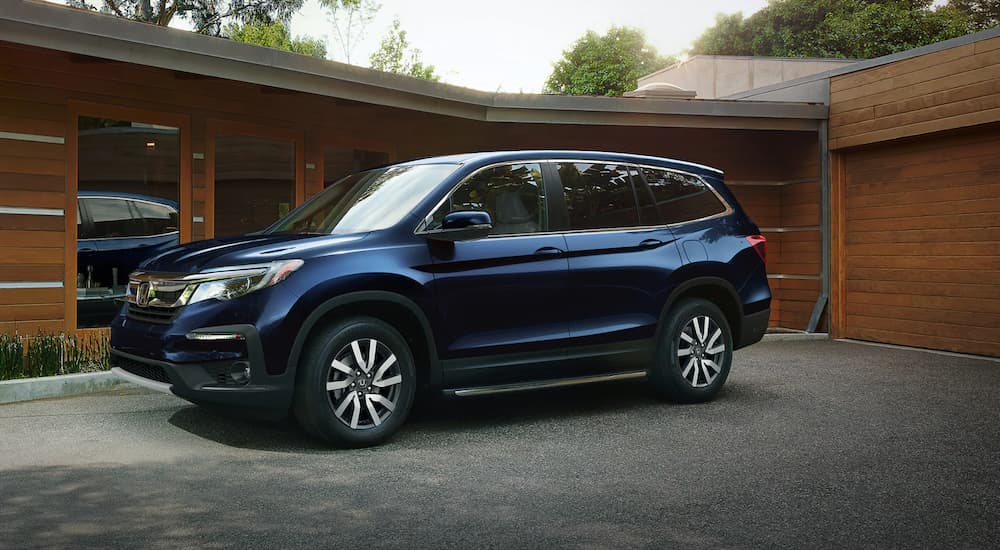A blue 2021 Honda Pilot EX-L is parked in front of a modern house.