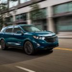 A teal 2021 Chevy Equinox is shown driving through the city after the 2021 Chevy Equinox vs 2021 Honda CR-V comparison.