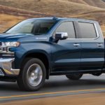 A blue 2021 Chevy Silverado 1500 is driving on an open road past a vineyard.