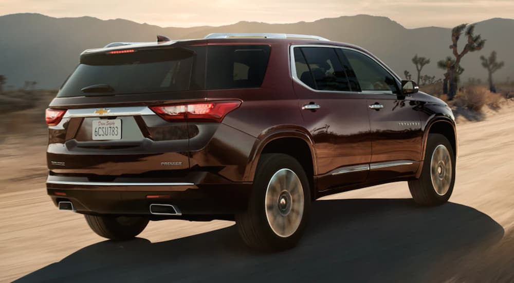 A maroon 2021 Chevy Traverse is shown from the back driving on a desert road.