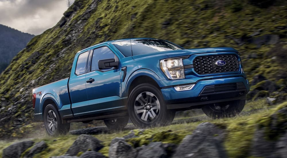 A blue 2021 Ford F-150 STX is shown driving past a rock face.