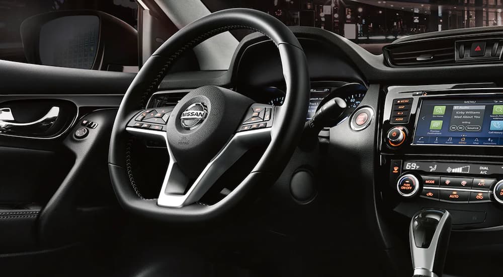 The black interior of a 2021 Nissan Rogue Sport shows the steering wheel and infotainment screen.