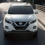 A white 2021 Nissan Rogue Sport is shown from the front driving on a highway.