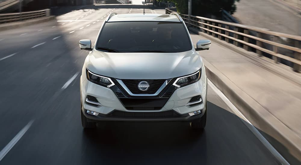 A white 2021 Nissan Rogue Sport is shown from the front driving on a highway.