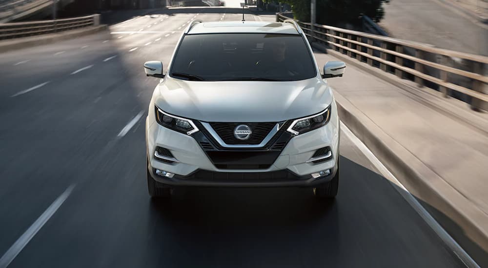 A white 2021 Nissan Rogue Sport is shown driving on a highway.