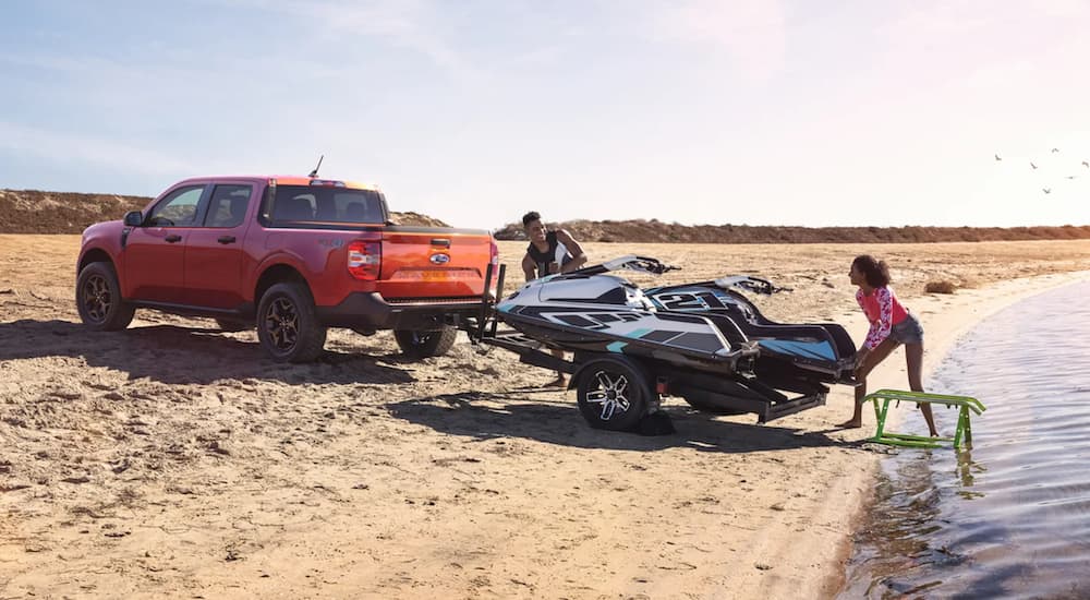 An orange 2022 Ford Maverick is shown towing a jet ski on the beach.