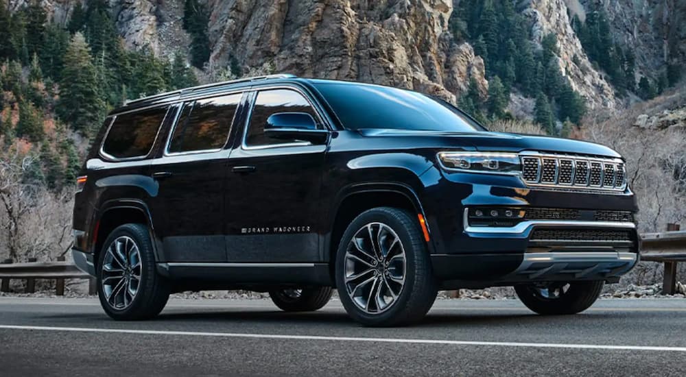 A black 2022 Grand Wagoneer is shown from the side driving on a highway in the mountains.