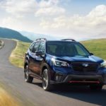 A dark blue 2021 Subaru Forester is shown driving past a field after leaving a Subaru Forester dealership.