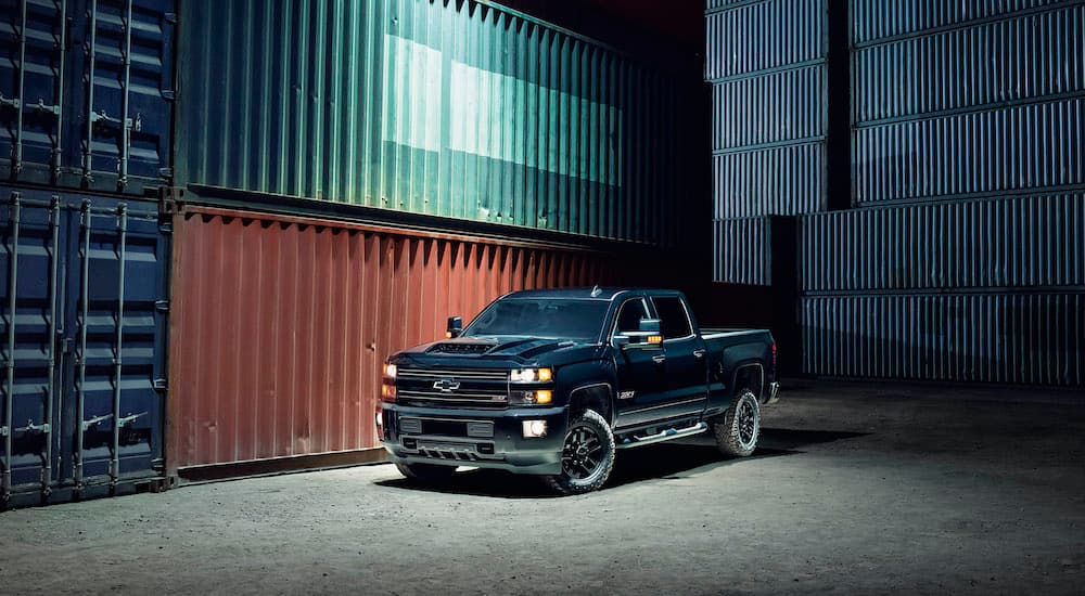 A black 2017 Chevy Silverado 2500HD is shown parked next to shipping containers after leaving a used Chevy truck dealership