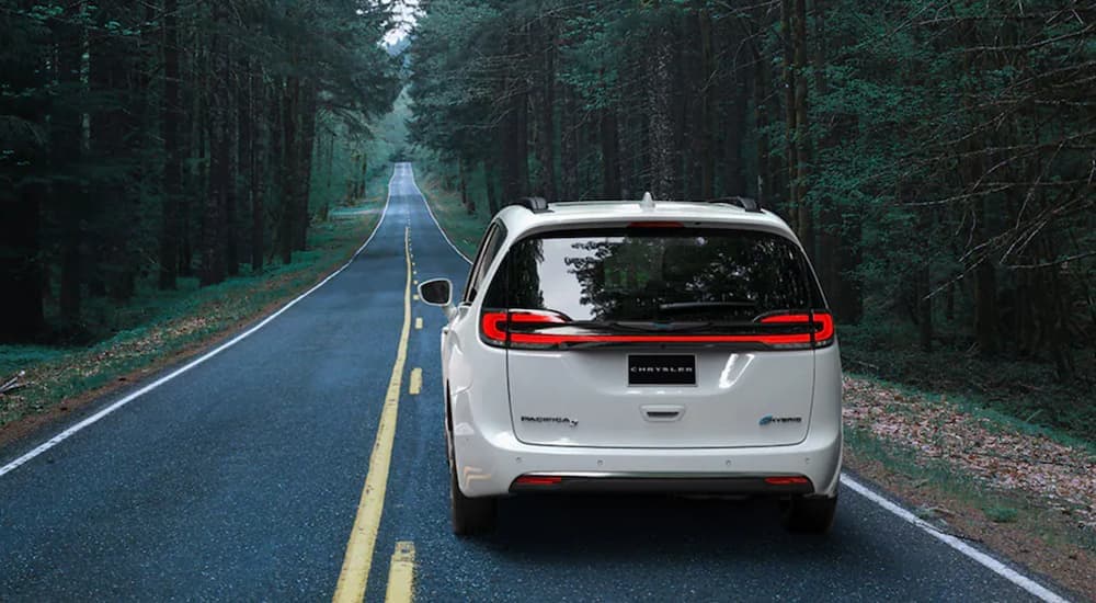 A white 2020 used Chrysler Pacifica Hybrid is shown from the back driving down an open road.