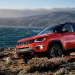 A red 2020 Jeep Compass Trailhawk, that can be found at one of your local used car dealerships, is shown parked next to the ocean.