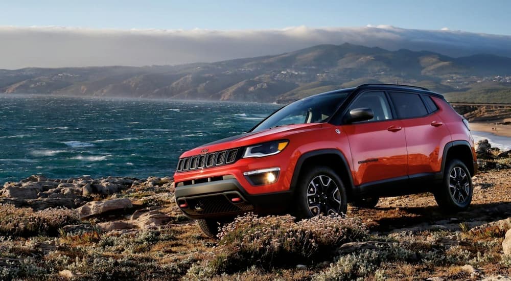 A red 2020 Jeep Compass Trailhawk, that can be found at one of your local used car dealerships, is shown parked next to the ocean.