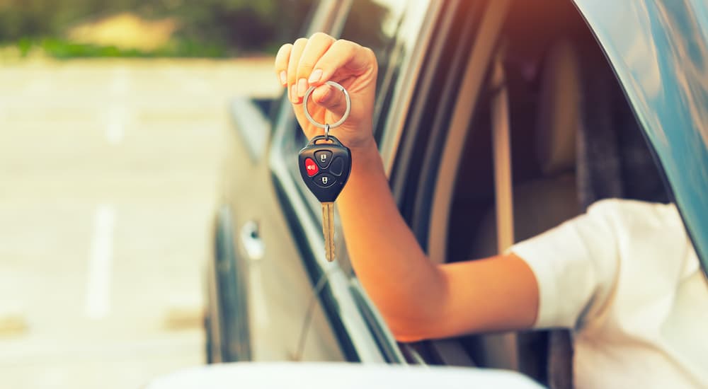 A person is holding out a set of car keys through a passenger window.