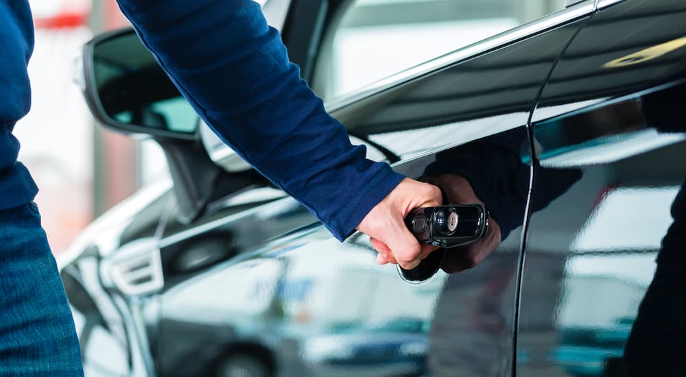 A person is opening a car door at a used car lot.