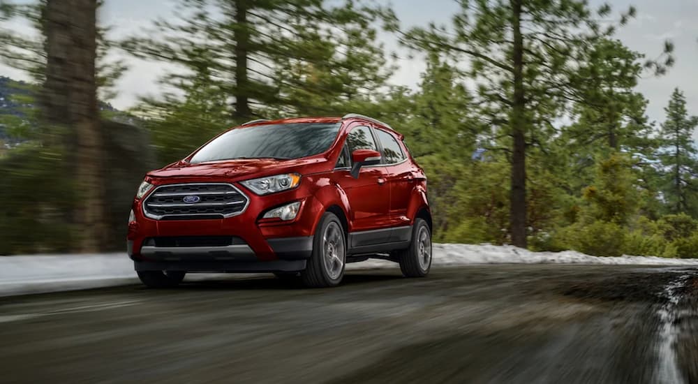 A red 2021 Ford EcoSport is shown driving on a tree lined road.