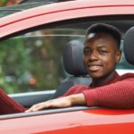 A teen driver is sitting in the front seat of a red car after looking at a 2021 Nissan Altima vs 2021 Honda Accord comparison.