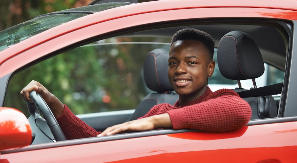 A teen driver is sitting in the front seat of a red car after looking at a 2021 Nissan Altima vs 2021 Honda Accord comparison.