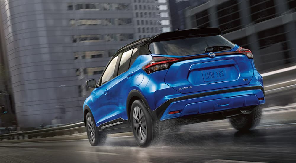 A blue 2021 Nissan Kicks is shown from the rear driving through a rainy city.