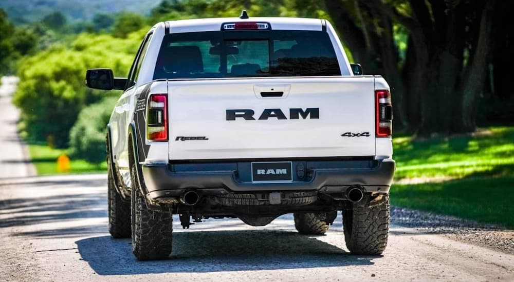 A white 2021 Ram 1500 is shown from the rear driving down a an open road.