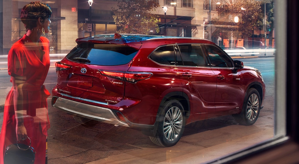 A red 2021 Toyota Highlander Platinum Hybrid is shown through the glass of a store front.