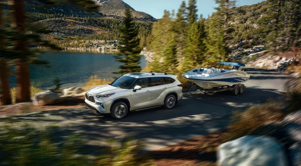 A white 2021 Toyota Highlander XLE is shown towing a boat past a lake.
