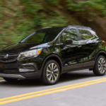 A black 2022 Buick Encore is shown from the side driving on a tree lined road.