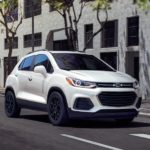 A white 2022 Chevy Trax is shown driving through a city.