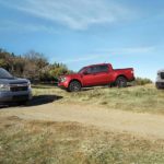 A blue, red and grey 2022 Ford Maverick are shown parked in a field under a blue sky.