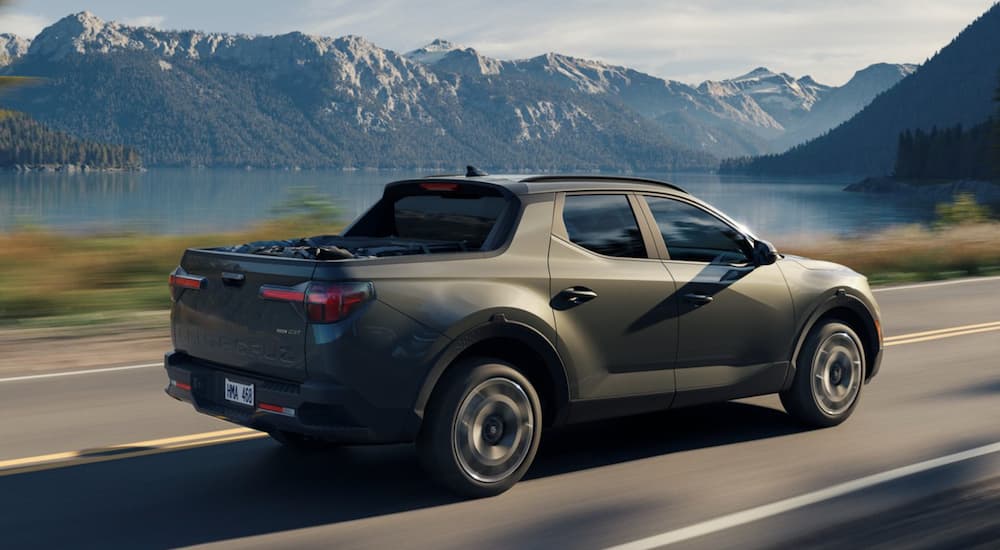 A green 2022 Hyundai Santa Cruz is shown from the rear driving on an open road past a lake.