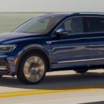 A blue 2021 Volkswagen Tiguan is shown driving over a bridge.