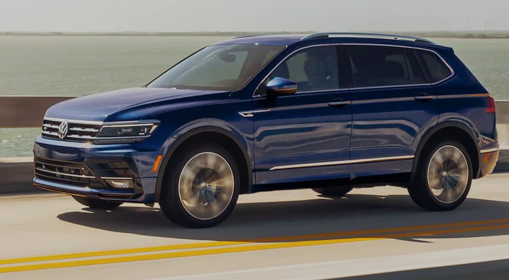 A blue 2021 Volkswagen Tiguan is shown driving over a bridge.