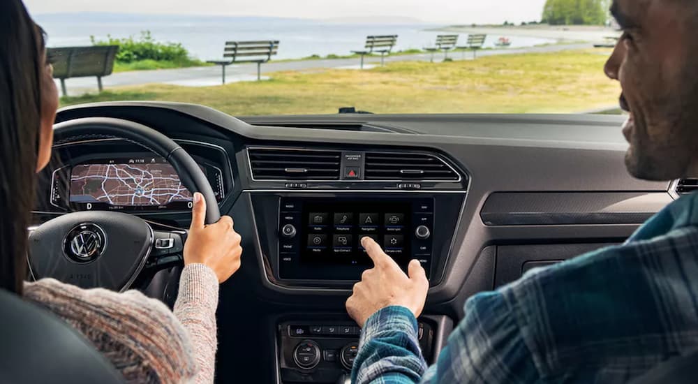The interior of a 2022 Volkswagen Tiguan shows the steering wheel and infotainment screen with two passengers in the front seats.