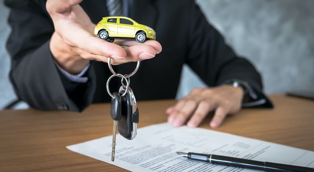 A salesperson is holding out a toy car and a set of keys during a Chevy lease deal.