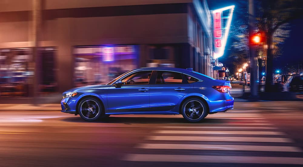 A blue 2022 Honda Civic Touring Sedan is shown from the side driving through a city at night.