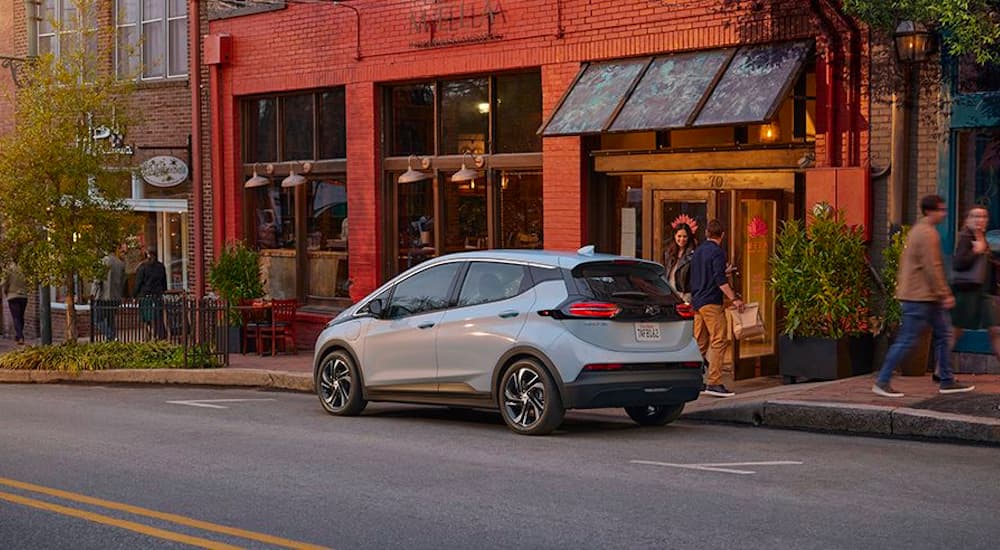 A pale blue 2022 Chevy Bolt EV is shown parked in front of a shop.