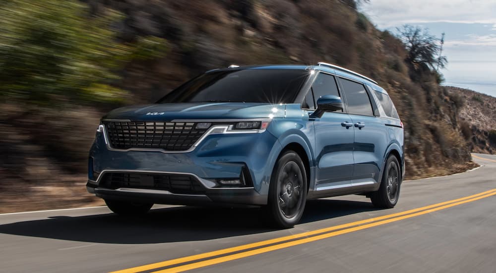 A blue 2022 Kia Carnival is shown driving from a low angle.