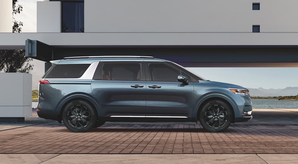 A blue 2022 Kia Carnival is shown from the side parked in front of a modern building after leaving a Kia Dealership.