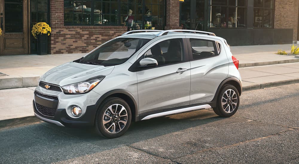 A silver 2021 Chevy Spark is shown parked in front of a shop.
