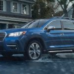 A blue 2021 Subaru Ascent is shown driving through the rain in a suburban neighborhood.